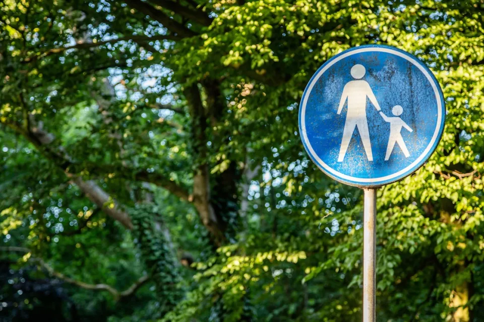 Blue sign with white sillhouettes indicating parent and child crossing street.